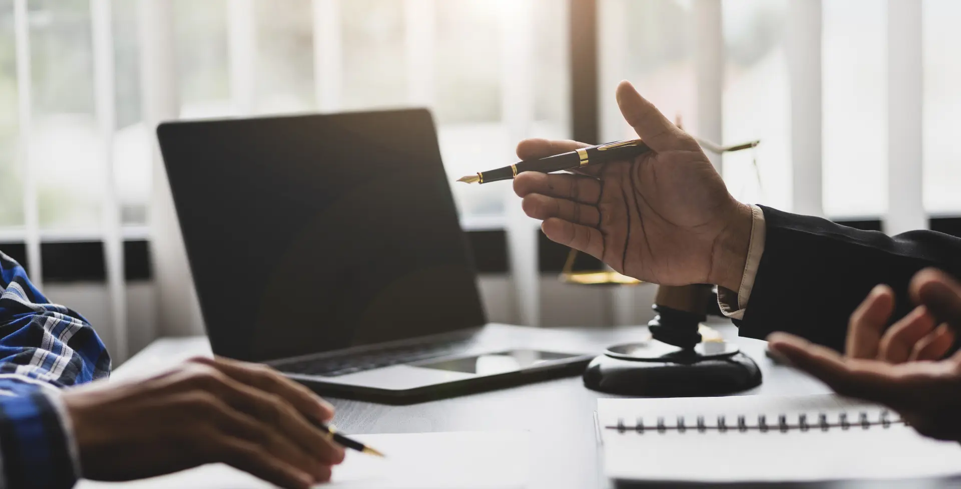 Arbitration Services, Inc. Two people in a meeting with a laptop and documents on a table, one holds a pen gesturing, while the other listens.